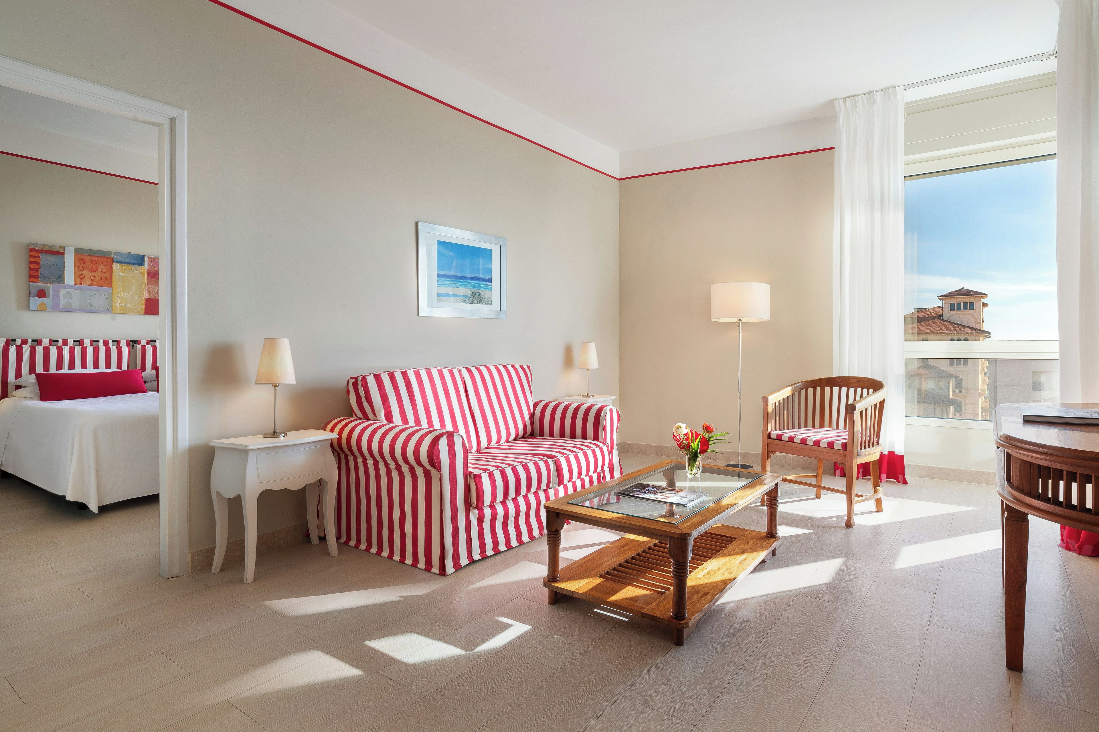 A hotel room with a bed, a striped sofa, a coffee table, a chair, a lamp, and a window with a view.