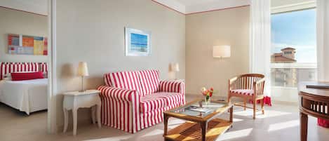 A hotel room with a bed, a striped sofa, a coffee table, a chair, a lamp, and a window with a view.