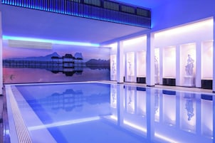 Una piscina interior moderna con agua cristalina, rodeada de paredes blancas e iluminada por luces azules.