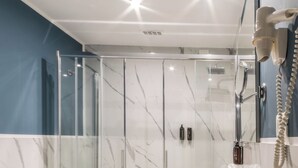 Un baño moderno con ducha de vidrio, un lavamanos grande y un mueble de tocador con artículos de aseo.