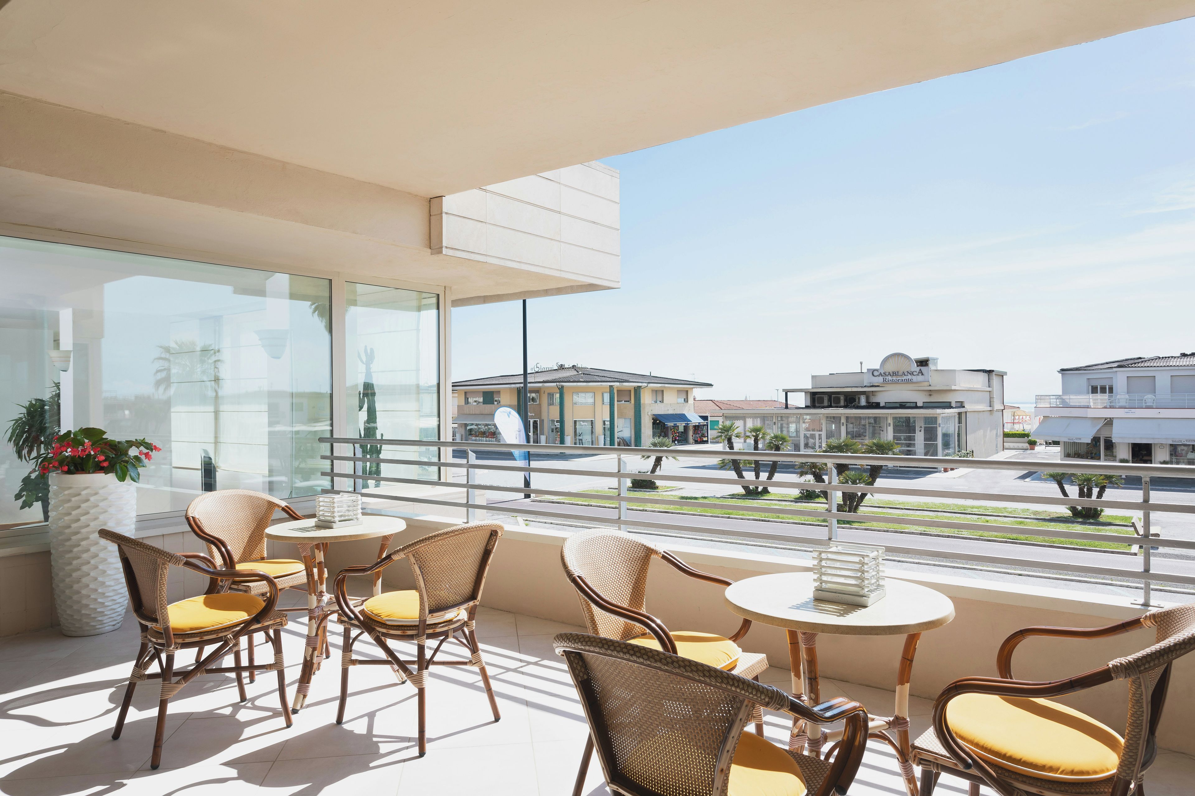 A balcony with wicker chairs and a table, overlooking a street with buildings.