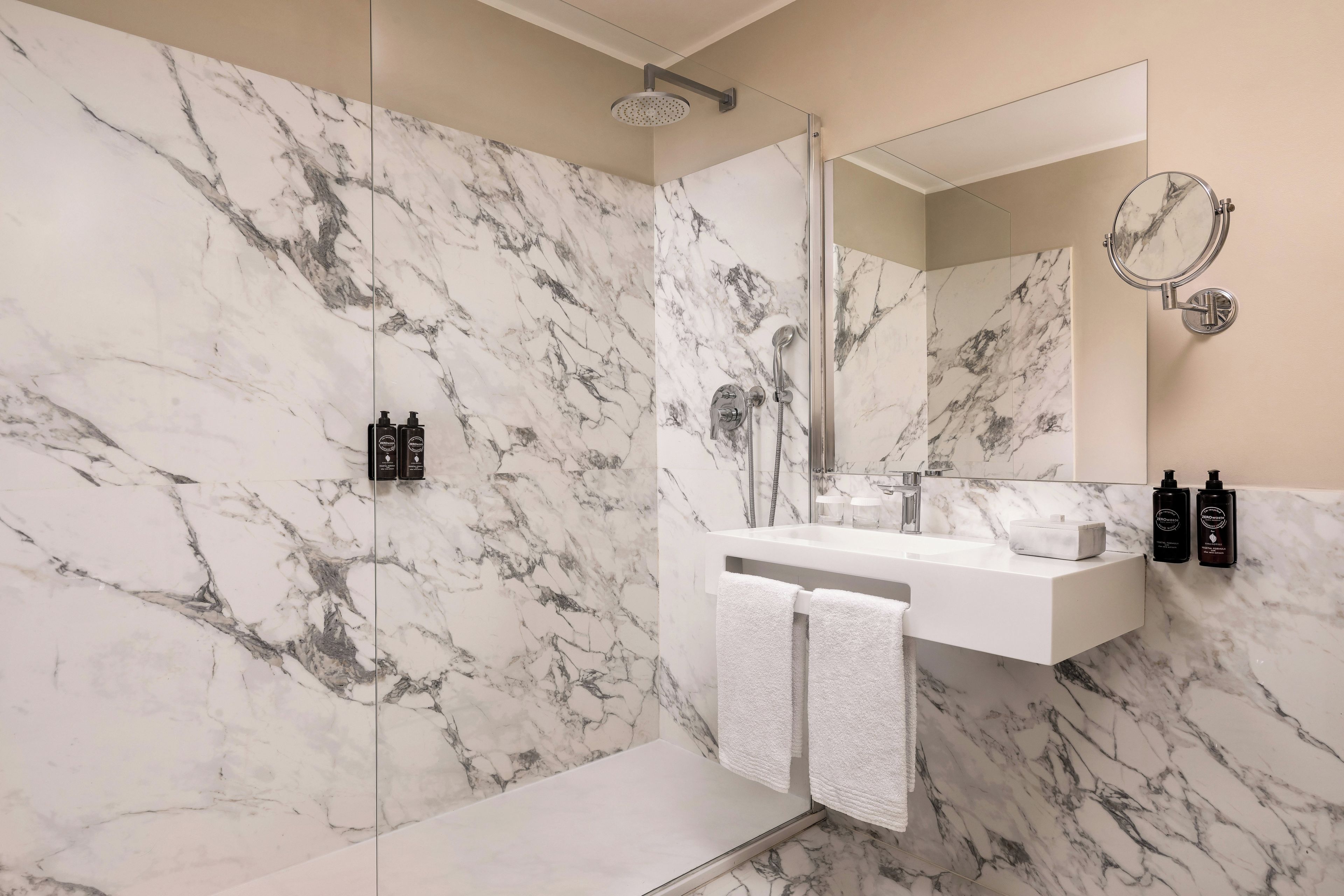 Un baño moderno con ducha de mármol, un espejo grande y un lavamanos blanco.