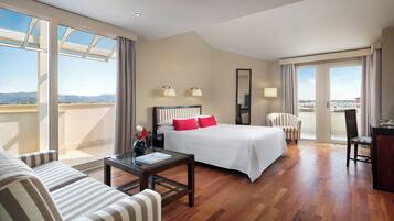 Habitación de hotel con cama, sofá, escritorio, silla y balcón con vistas.