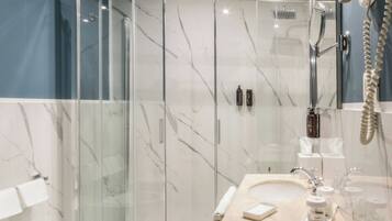 Un baño moderno con ducha de vidrio, lavamanos de mármol y tocador con artículos de aseo.