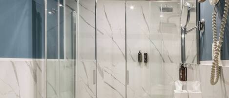 A modern bathroom with a glass-enclosed shower, a marble sink, and a vanity with toiletries.