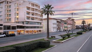 Un hotel de varios pisos con un llamativo letrero 'ASTOR', una calle bien cuidada y un cielo al atardecer.