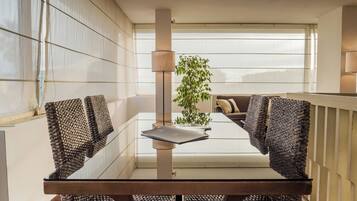Un espace repas moderne avec une table en verre, des chaises en osier, une plante en pot et une vue par la fenêtre.