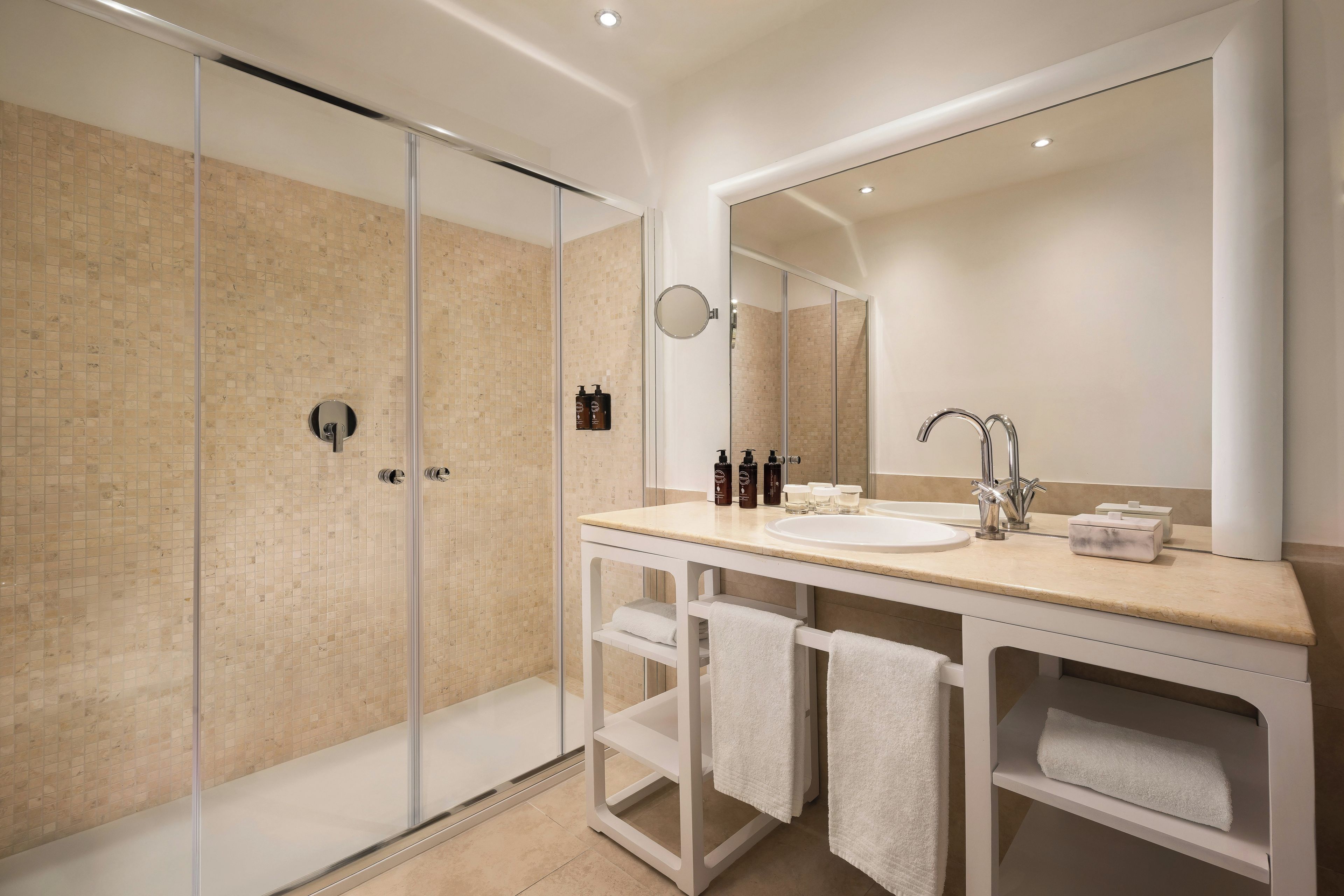 Un baño moderno con cabina de ducha de vidrio, un espejo grande y un lavabo con toalleros.