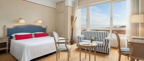 Habitación de hotel con cama, dos sillas, una mesita, un sofá y vistas al mar.