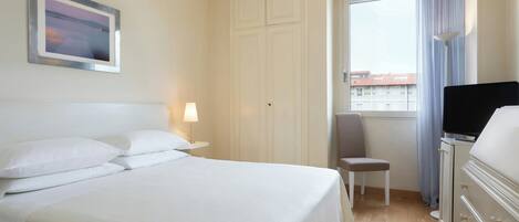 A hotel room with a bed, a chair, a television, and a window with curtains.