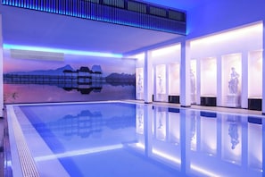A modern indoor pool with clear water, surrounded by white walls and illuminated by blue lighting. - Sina Astor (Viareggio)