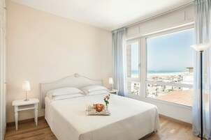 A hotel room with a bed, a bedside table, a lamp, a tray with breakfast, and a view of the beach.