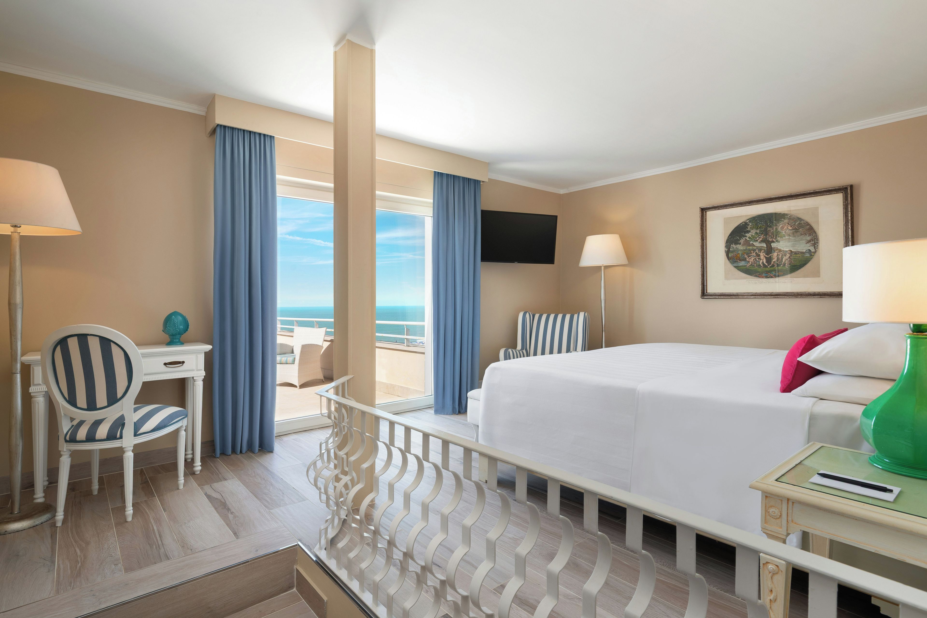 A hotel room with a bed, a desk, a chair, a TV, and a balcony with curtains.