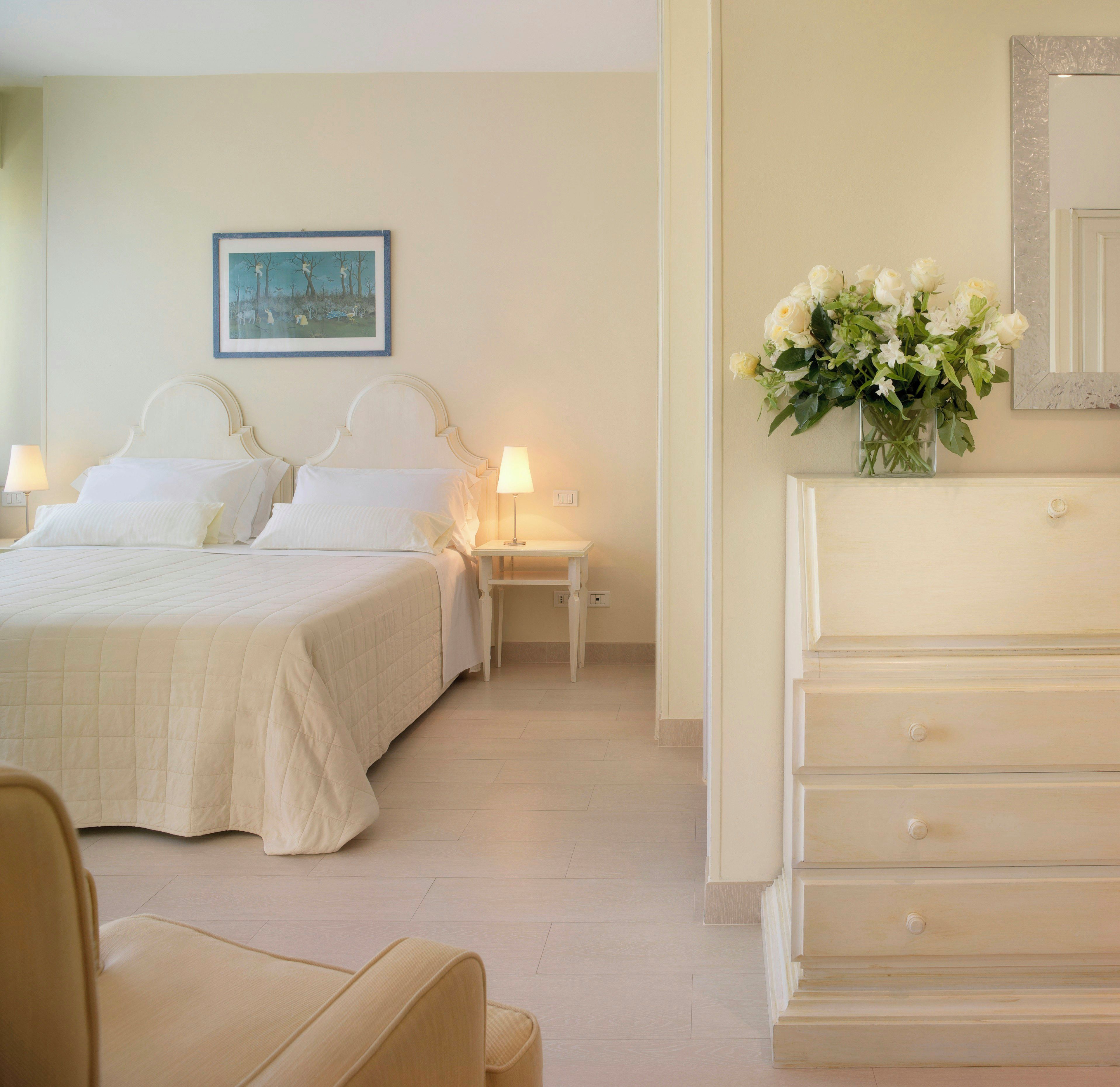 Una habitación de hotel con cama, mesitas de noche, cómoda, silla y un cuadro en la pared.