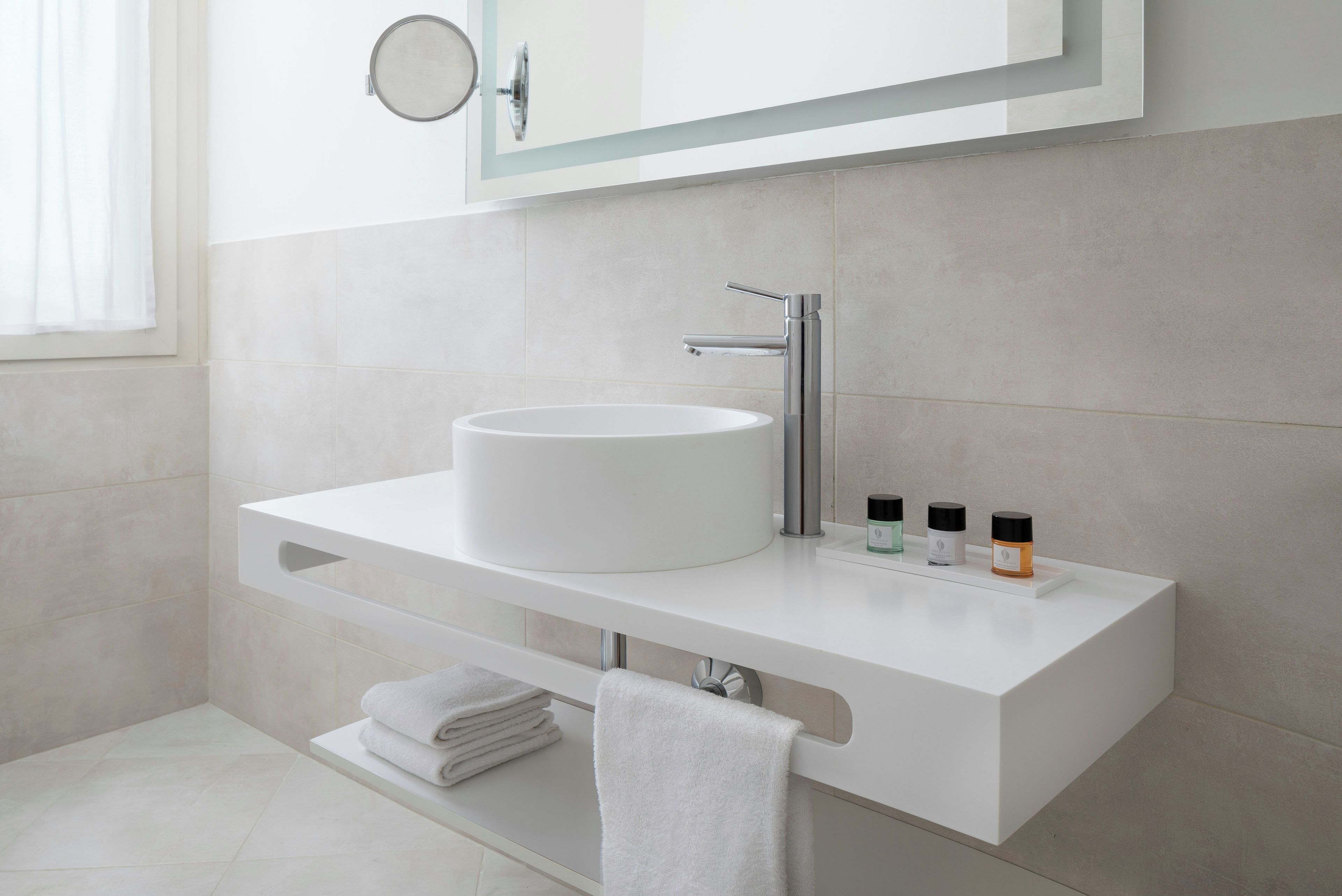 Une salle de bain moderne avec un meuble-lavabo blanc, un lavabo rond, un miroir et un porte-serviettes.