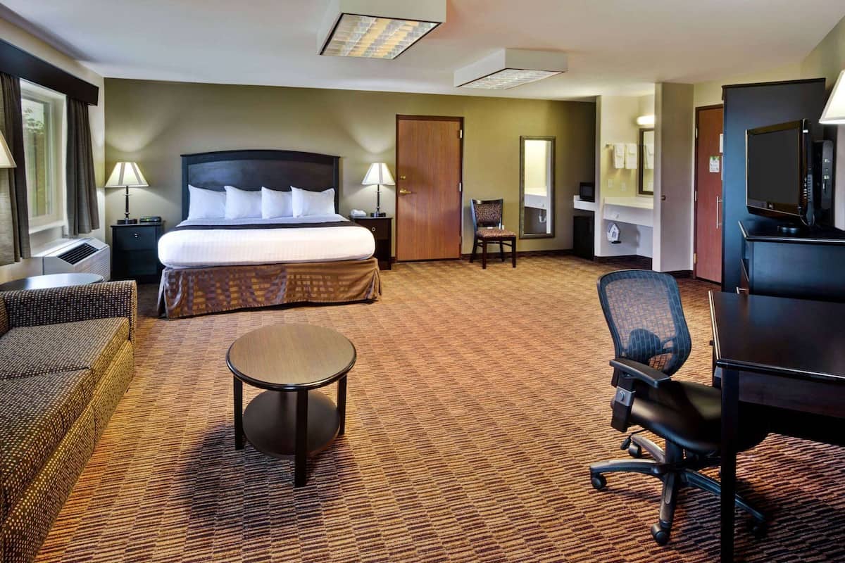A hotel room with a bed, a round table, a sofa, a chair, a television, and a desk.