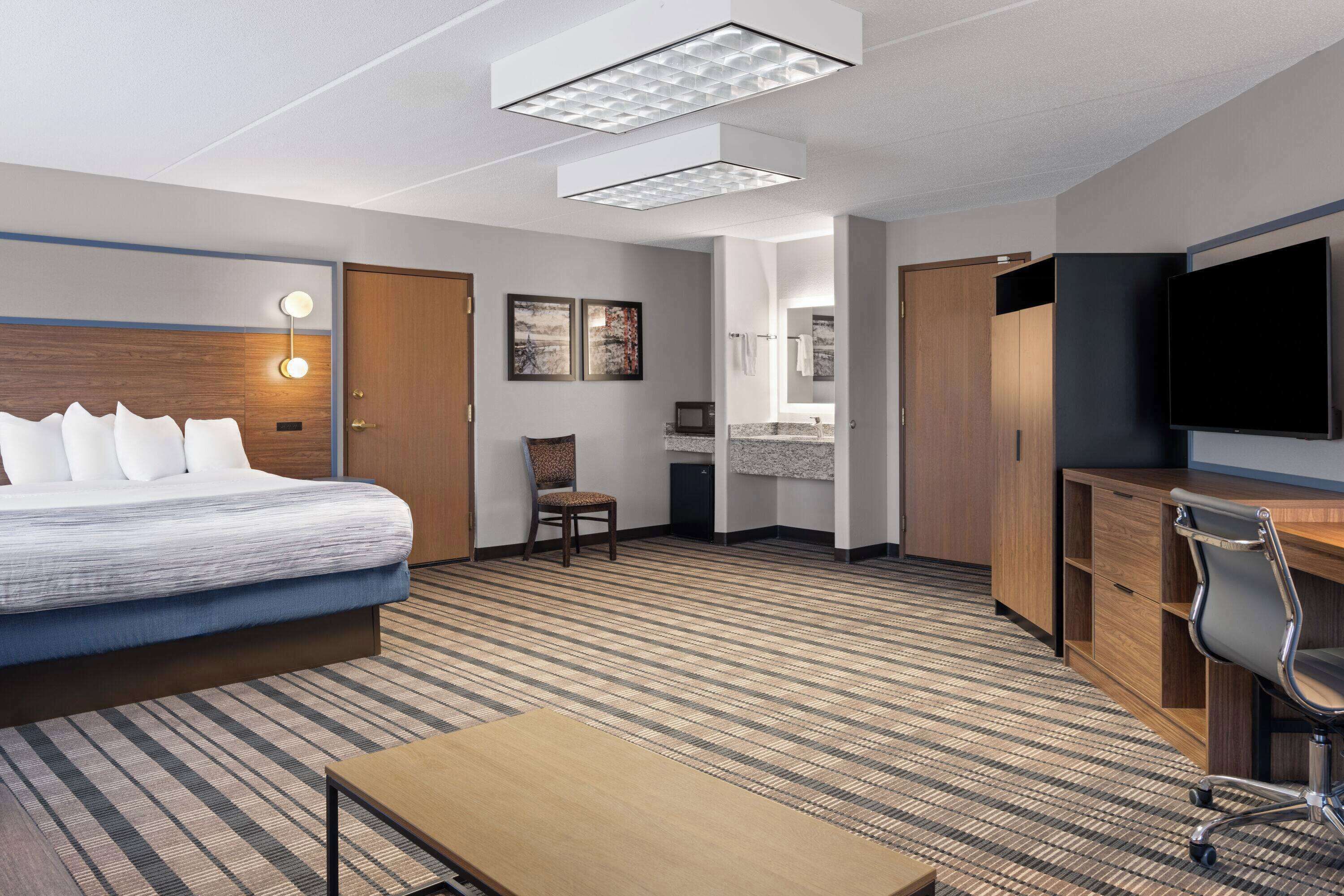 A hotel room with a bed, a desk, a chair, a TV, and a bathroom.