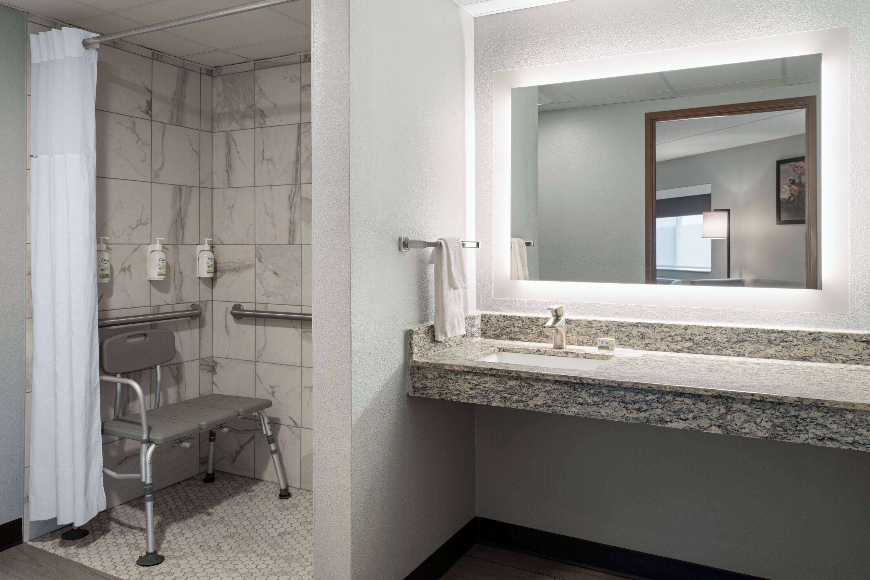 A bathroom with a shower, grab bar, and a sink with a mirror.