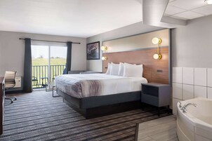 Quarto de hotel moderno com uma cama grande, uma escrivaninha, uma cadeira, banheiro com banheira e varanda com vista.