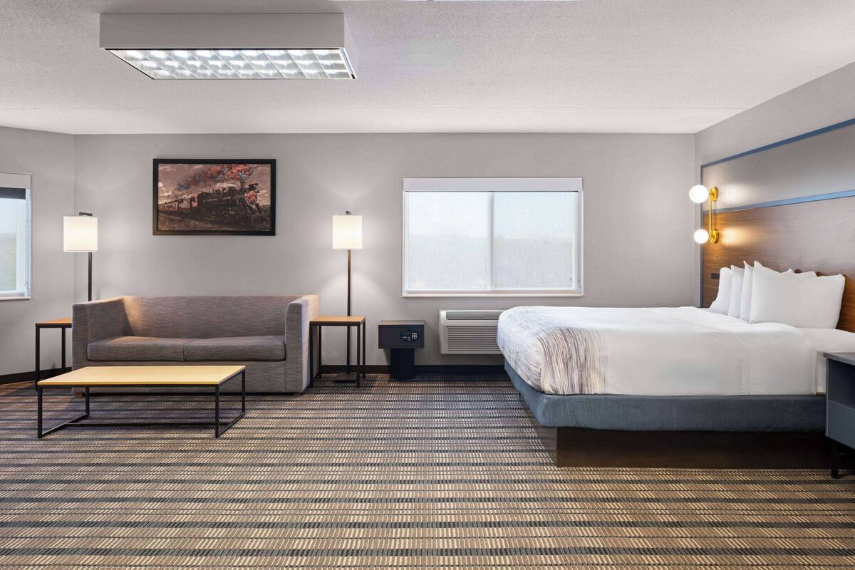 A hotel room with a bed, a sofa, a small table, a lamp, and a picture on the wall.