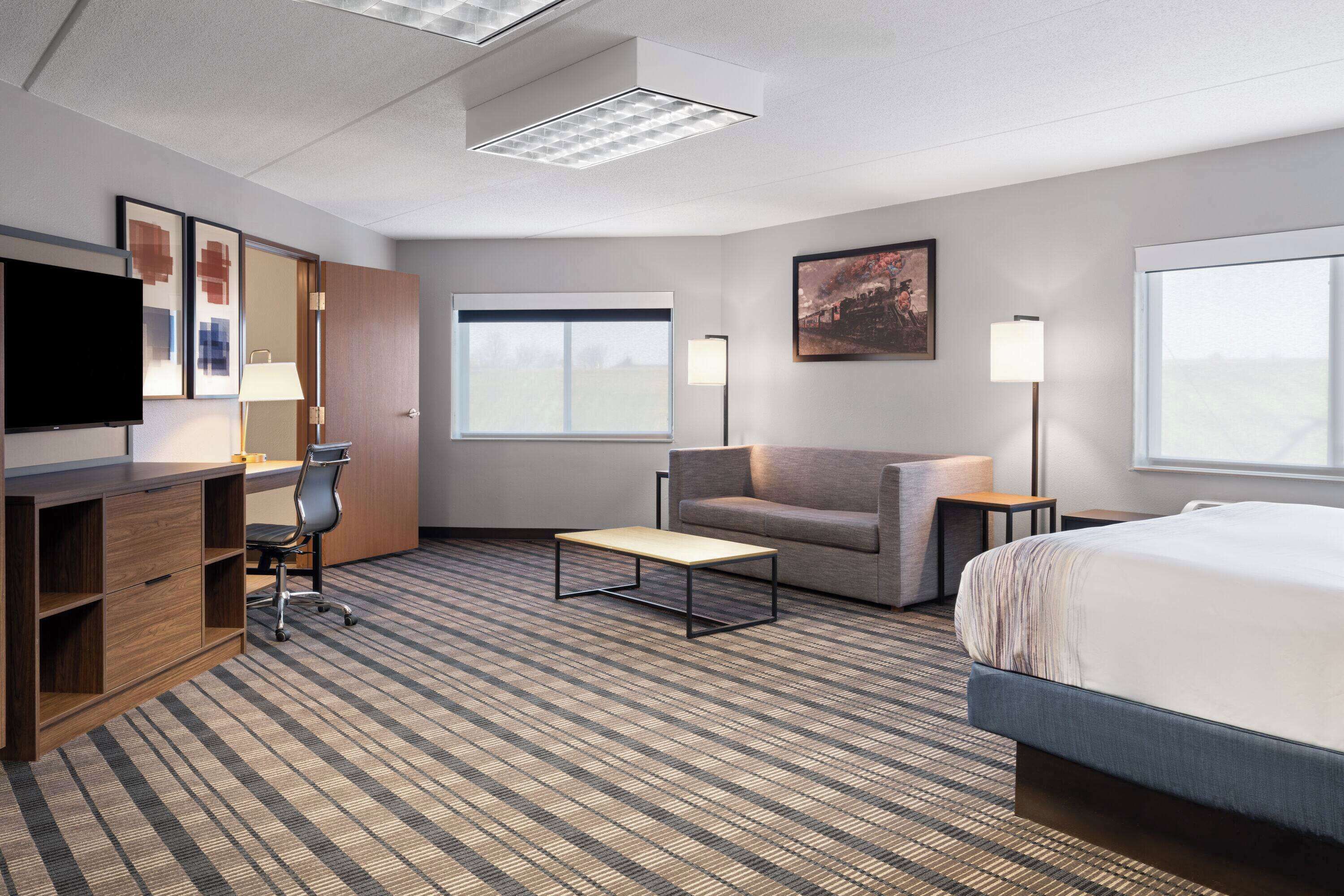Habitación de hotel con cama, escritorio, silla, sofá, televisor y ventana.