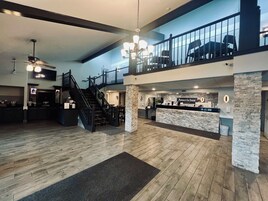 Um hall de hotel espaçoso com piso de madeira, balcão de recepção, escada e varanda com cadeiras.