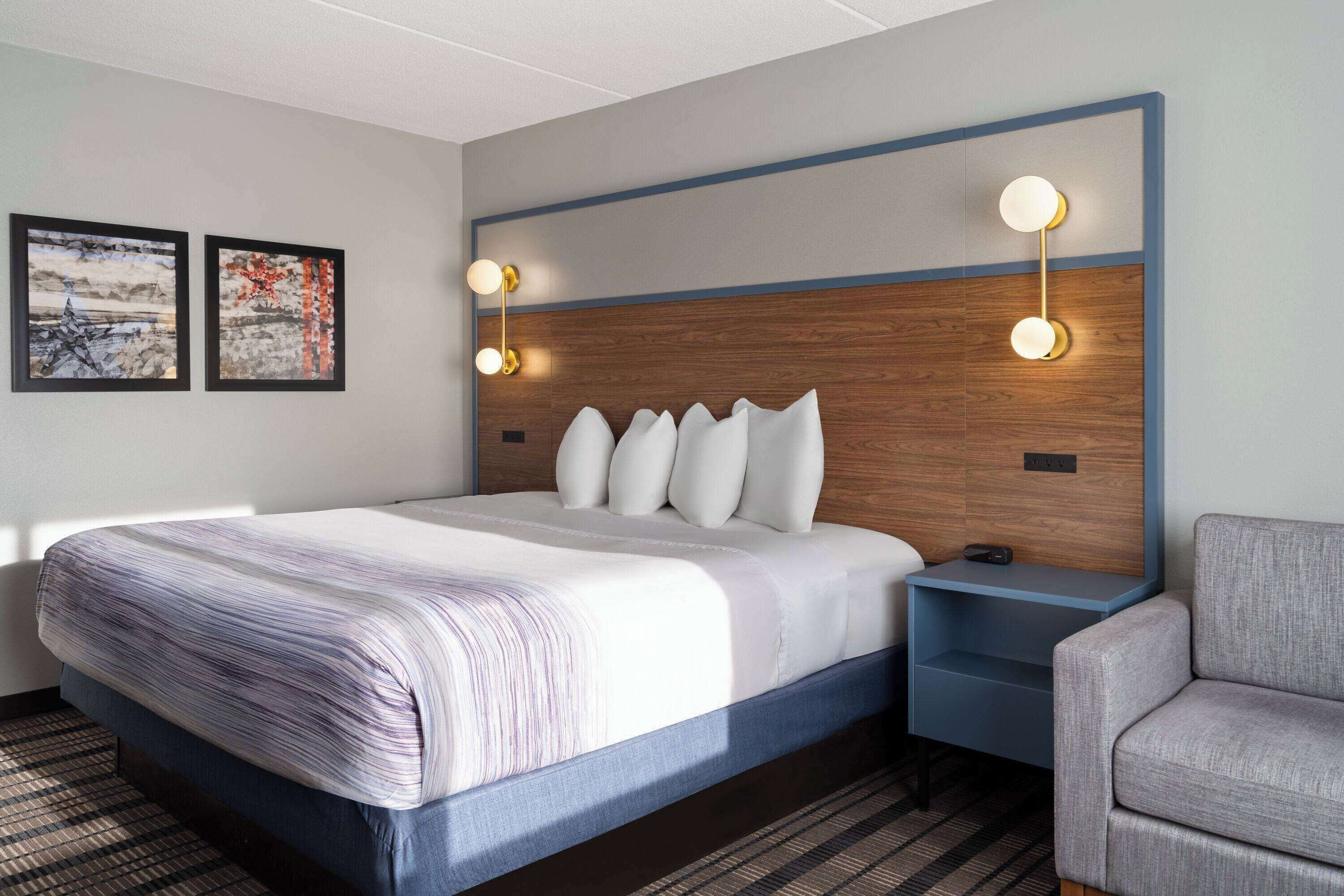 A hotel room with a large bed, a nightstand, a chair, and two wall-mounted light fixtures.