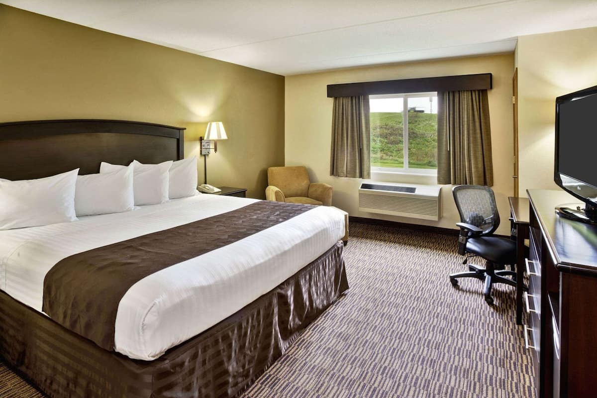 A hotel room with a large bed, a desk with a TV, a chair, a window with curtains, and an air conditioning unit.