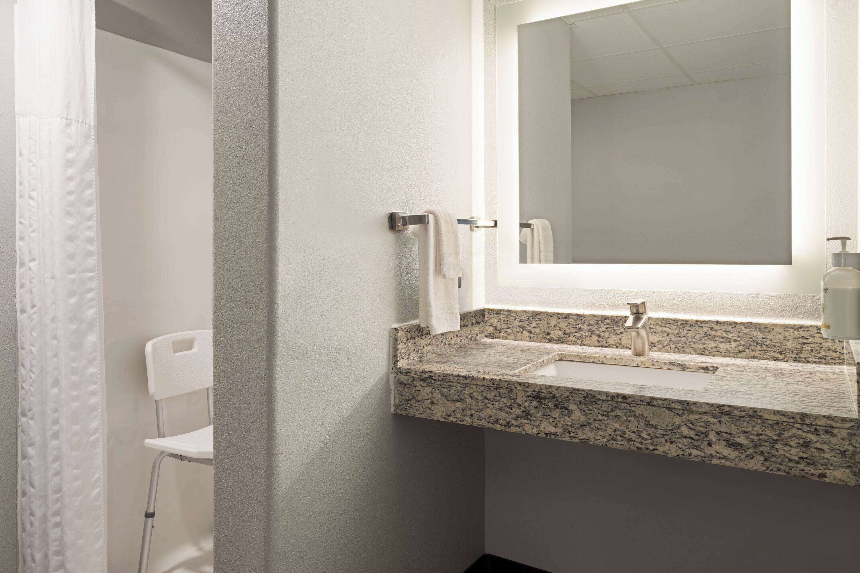 Une salle de bain avec un comptoir en granit, un miroir et une chaise blanche.