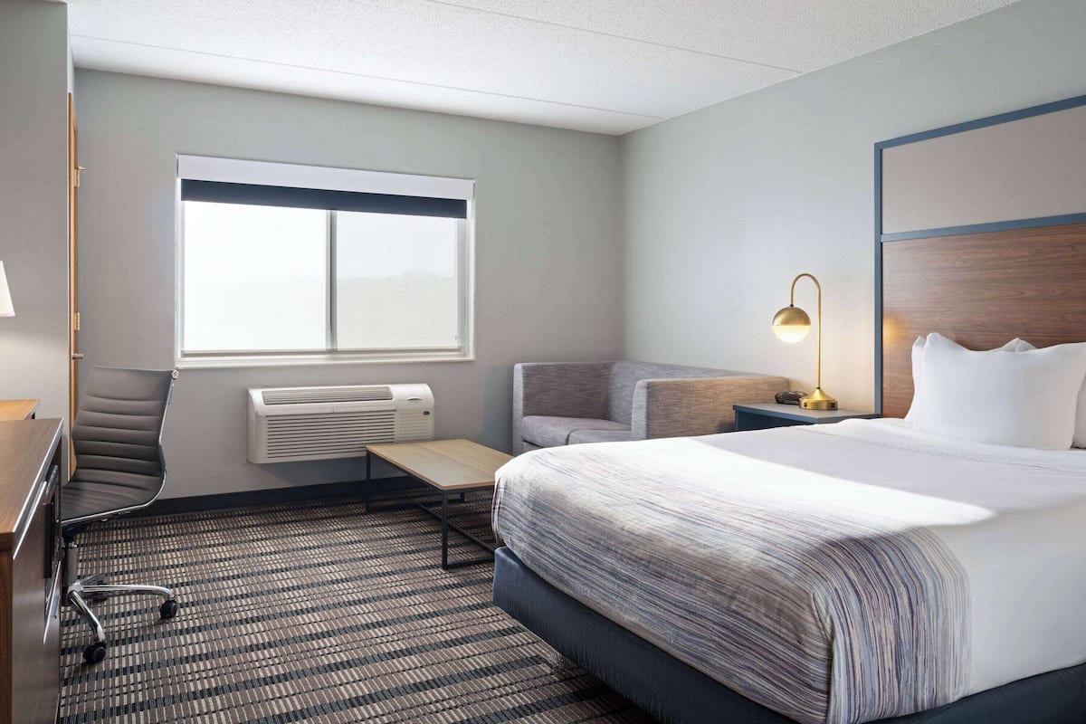 A hotel room with a large bed, a desk, a chair, a window, and a lamp.