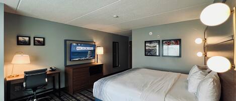 A hotel room with a bed, desk, chair, TV, and wall-mounted lights.