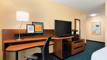 Habitación de hotel con escritorio de madera, televisor, lámpara, microondas, pequeño refrigerador y cama.