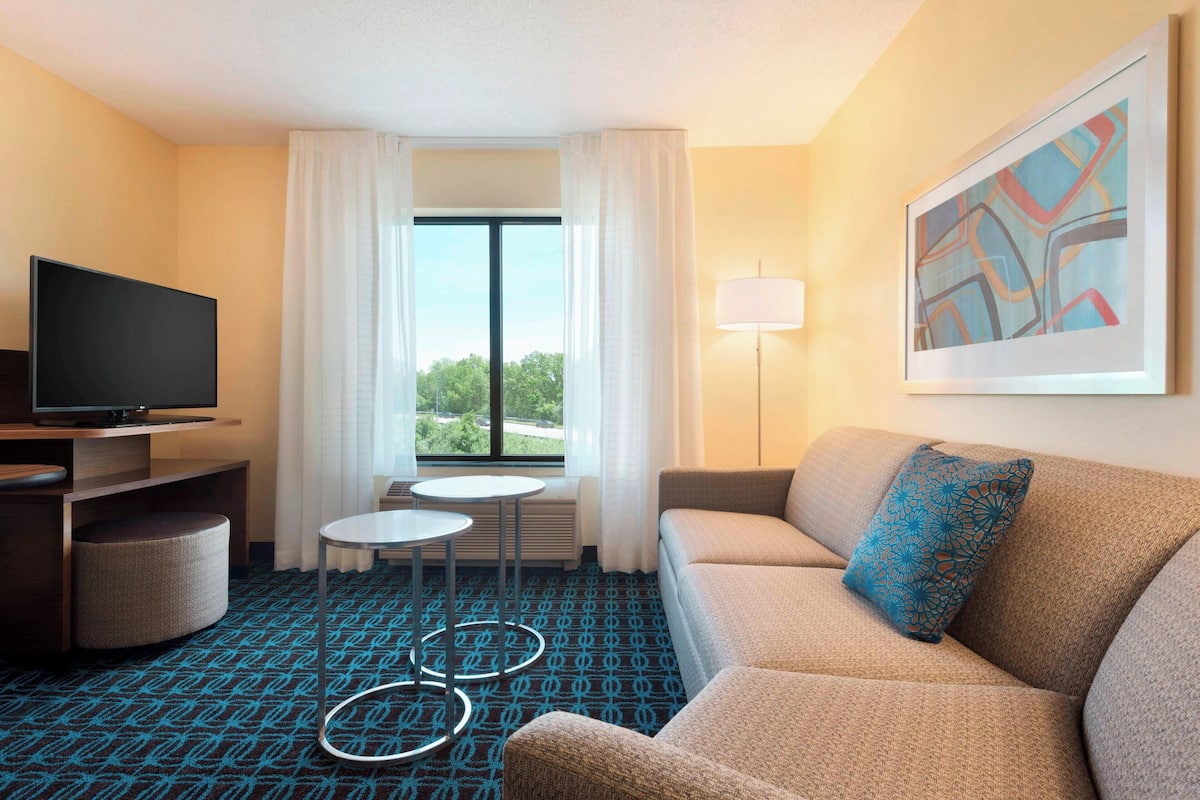 Une chambre d’hôtel avec un canapé, une télévision, une petite table et une fenêtre avec des rideaux.