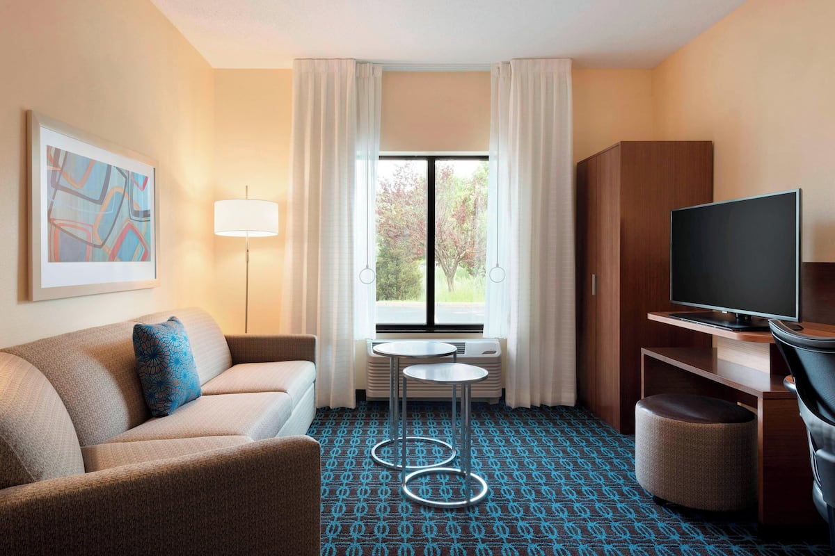 Une chambre d’hôtel avec un canapé, une télévision, une petite table et une fenêtre avec des rideaux.