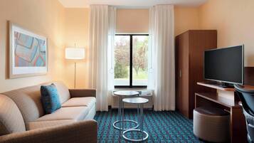 A hotel room with a sofa, a TV, a small table, and a window with curtains.