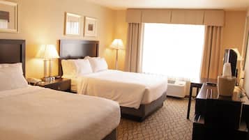 A hotel room with two beds, bedside lamps, a desk with a telephone, a TV, and a window with curtains.
