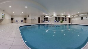 Una piscina interior con suelo de baldosas, zona de estar e iluminación empotrada en el techo.