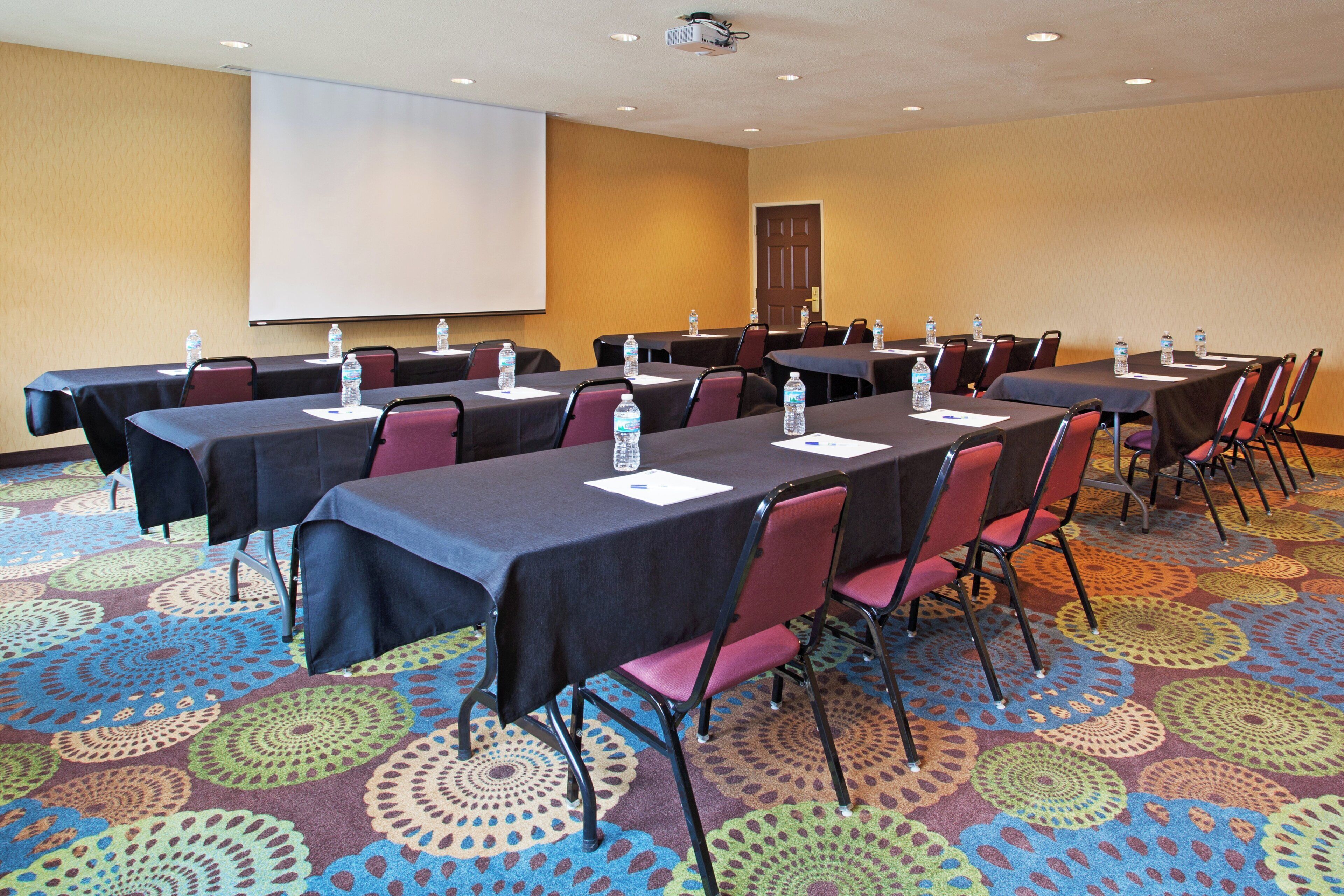 A conference room with tables, chairs, water bottles, and a projector screen.