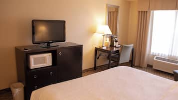 Habitación de hotel con cama, televisor, escritorio con lámpara, silla, microondas y cesto de basura.