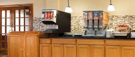 A breakfast bar with a coffee machine, juice dispensers, and a fruit display.
