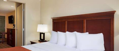 A hotel room with a large bed, a wooden headboard, a bedside table with a lamp, and a television on the wall.