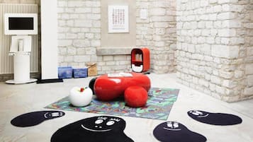 A room with a white brick wall, a red bean bag chair, a white table, and a black rug with smiley faces.