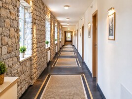 Un pasillo de hotel con paredes de piedra, puertas de madera y un largo corredor con suelo estampado.