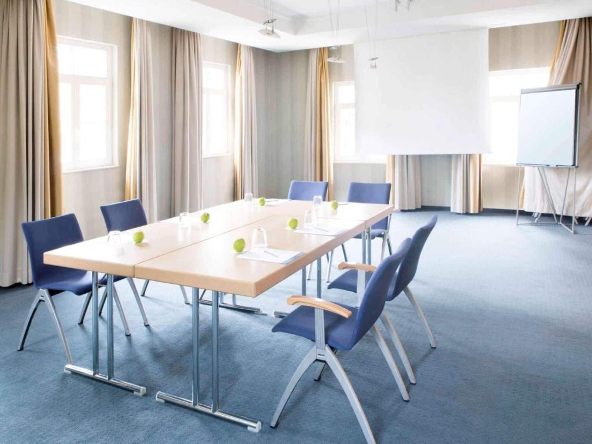 Un salón de conferencias con una mesa larga, sillas azules y una pizarra.