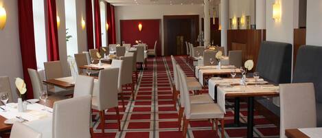 Un comedor de hotel con varias mesas y sillas, alfombra estampada y apliques de pared.