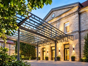 A hotel with a stone facade, a covered outdoor area with a metal framework, and potted plants.