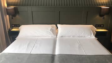 Een tweepersoonsbed met witte lakens, twee nachtkastjes met lampen, en een hoofdbord met verticale latten.