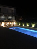 Una piscina circondata da poltroncine e ombrelloni, illuminata da luci soffuse.
