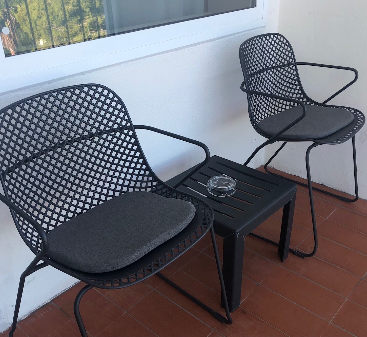 Dos sillas de malla negra con asientos y respaldos acolchados, una pequeña mesa negra y un vaso sobre la mesa.