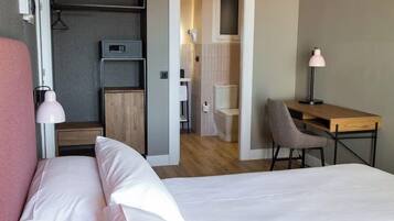 A hotel room with two beds, a desk, a chair, a wardrobe, and a small kitchenette.